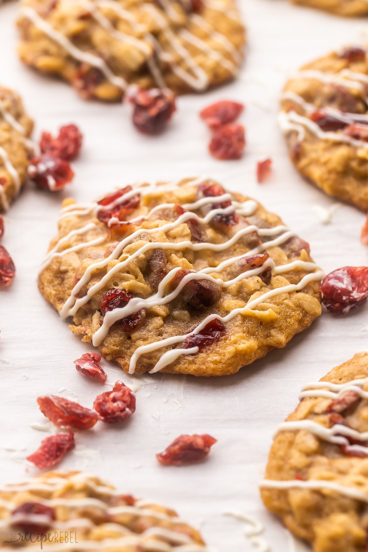 These chewy Oatmeal Cranberry Cookies are the perfect addition to your Christmas cookie trays! These cookies are made with rolled oats and dried cranberries, flavored with warm vanilla and cinnamon, and topped with a sweet white chocolate drizzle! #cookies #christmas #baking | christmas cookies | christmas baking | oatmeal cookies | cookie recipe | baking cookies | holiday baking | dried cranberries Top view of Oatmeal Cranberry Cookies on a white surface.