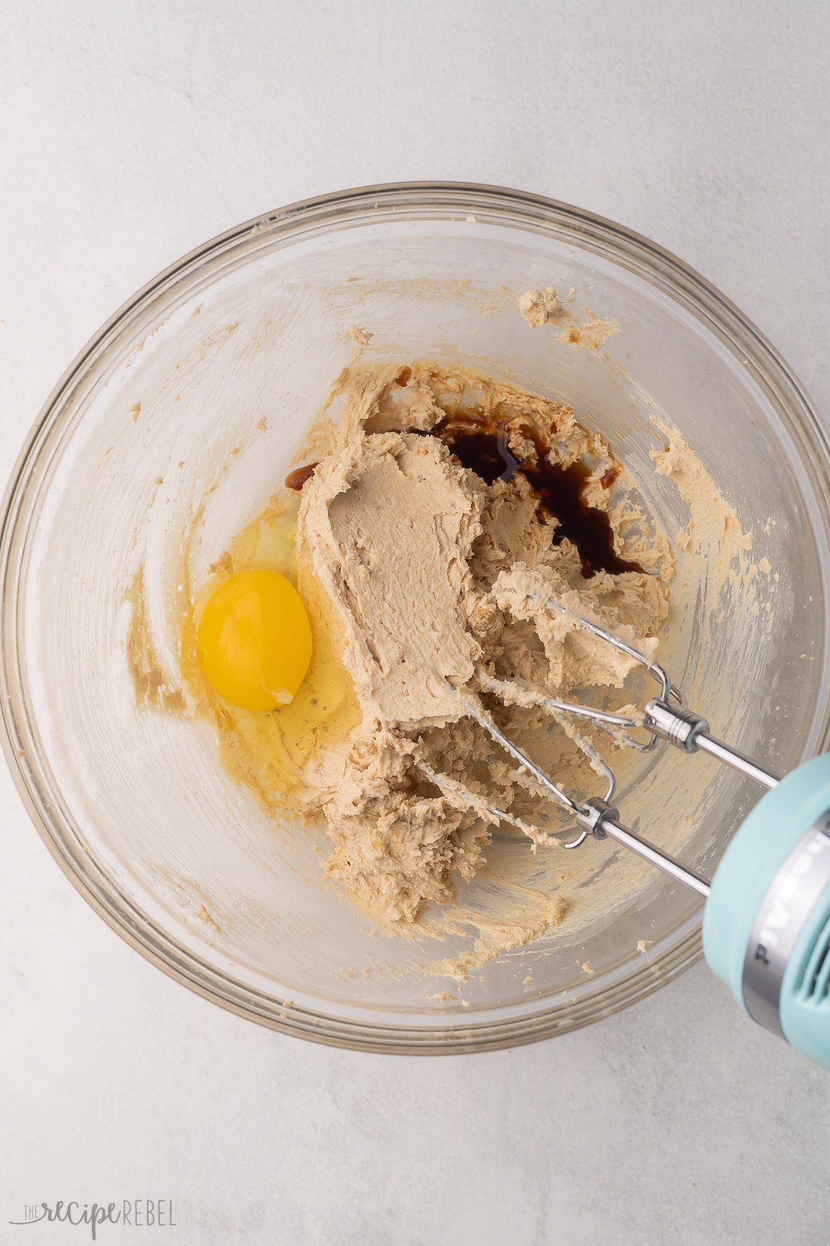 Top view of a glass mixing bowl with an egg and vanilla extract on top of creamed butter and sugar.