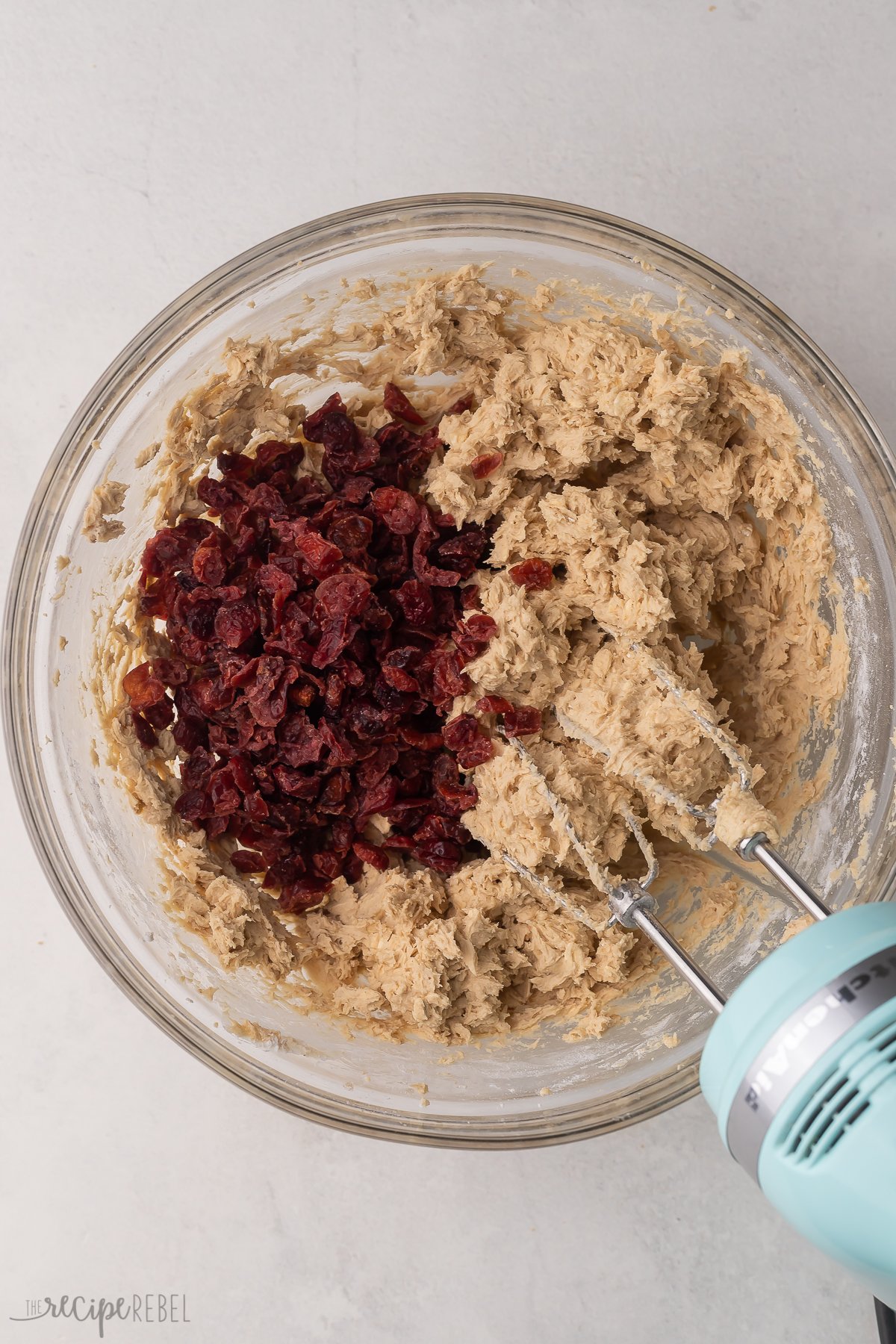 Top view of a glass mixing bowl with cookie dough in it and dried cranberries on top.