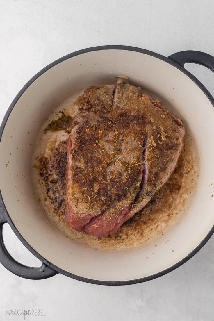 Top view of a Dutch oven with a seasoned beef roast being seared in it.