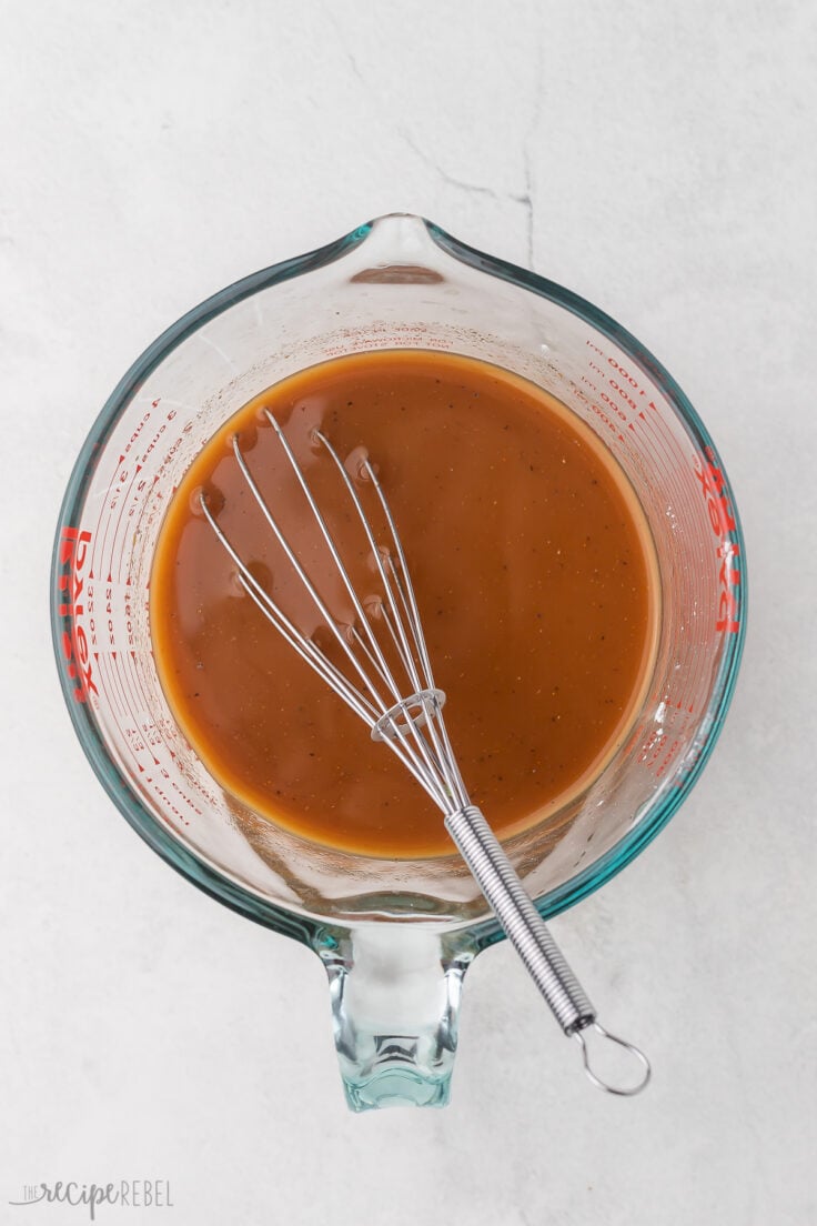 Top view of a glass measuring jug with broth and seasonings in it being whisked.