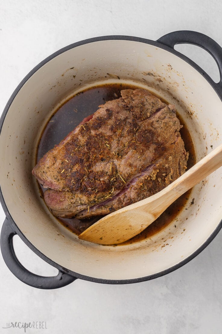 Top view of a Dutch oven with a beef roast in it, and a broth mixture on top.