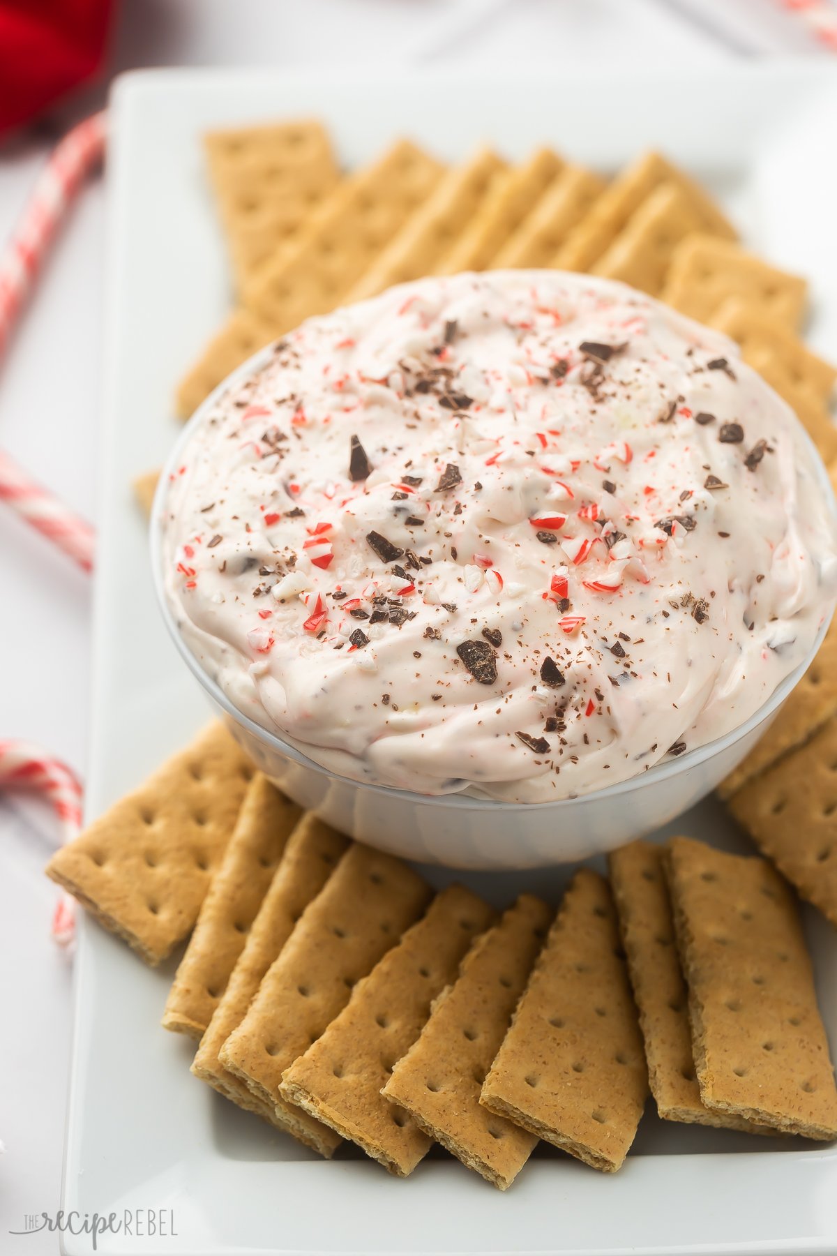 bowl of peppermint bark cheesecake dip on a white plater surrounded by graham crackers.