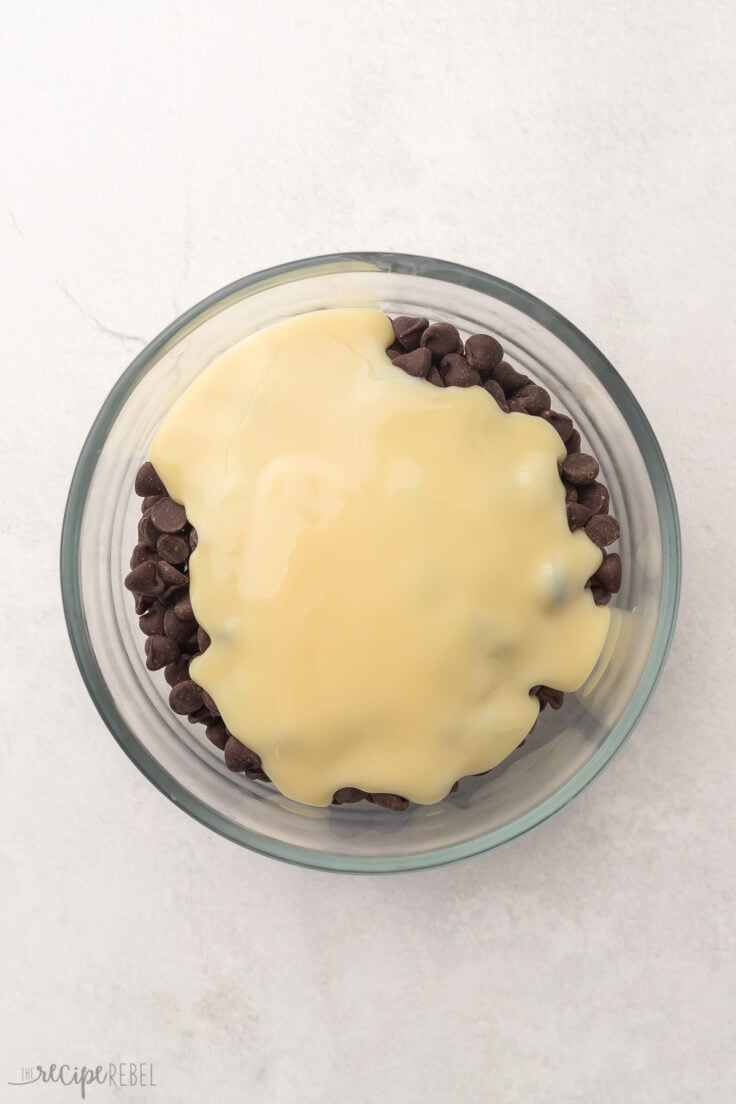 Top view of a glass mixing bowl with chocolate chips, peppermint extract, and evaporated milk on top.