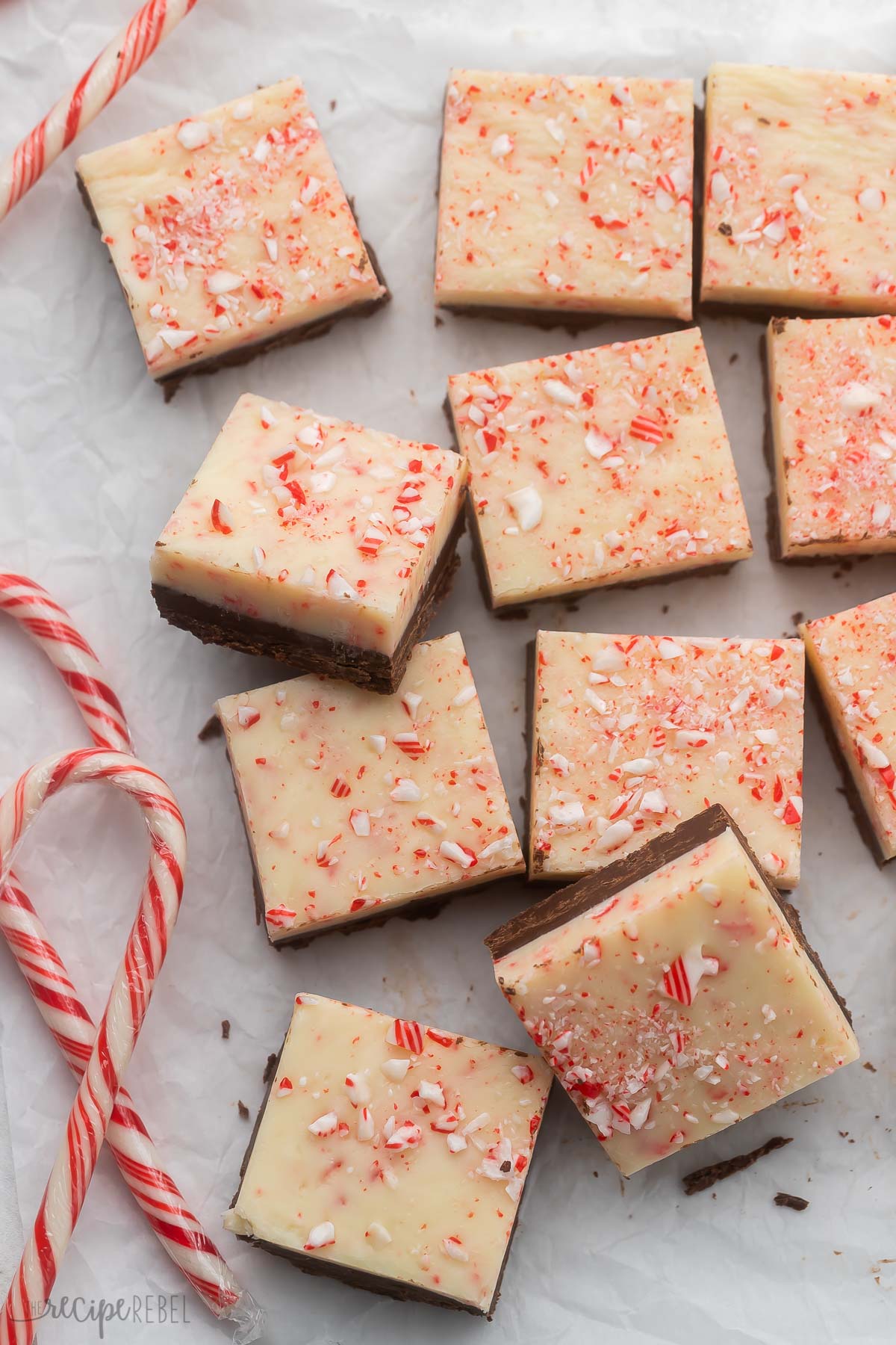 Top view of Close-up of a stack of Peppermint Bark Fudge cut into squares on a white surface with candy canes around it.