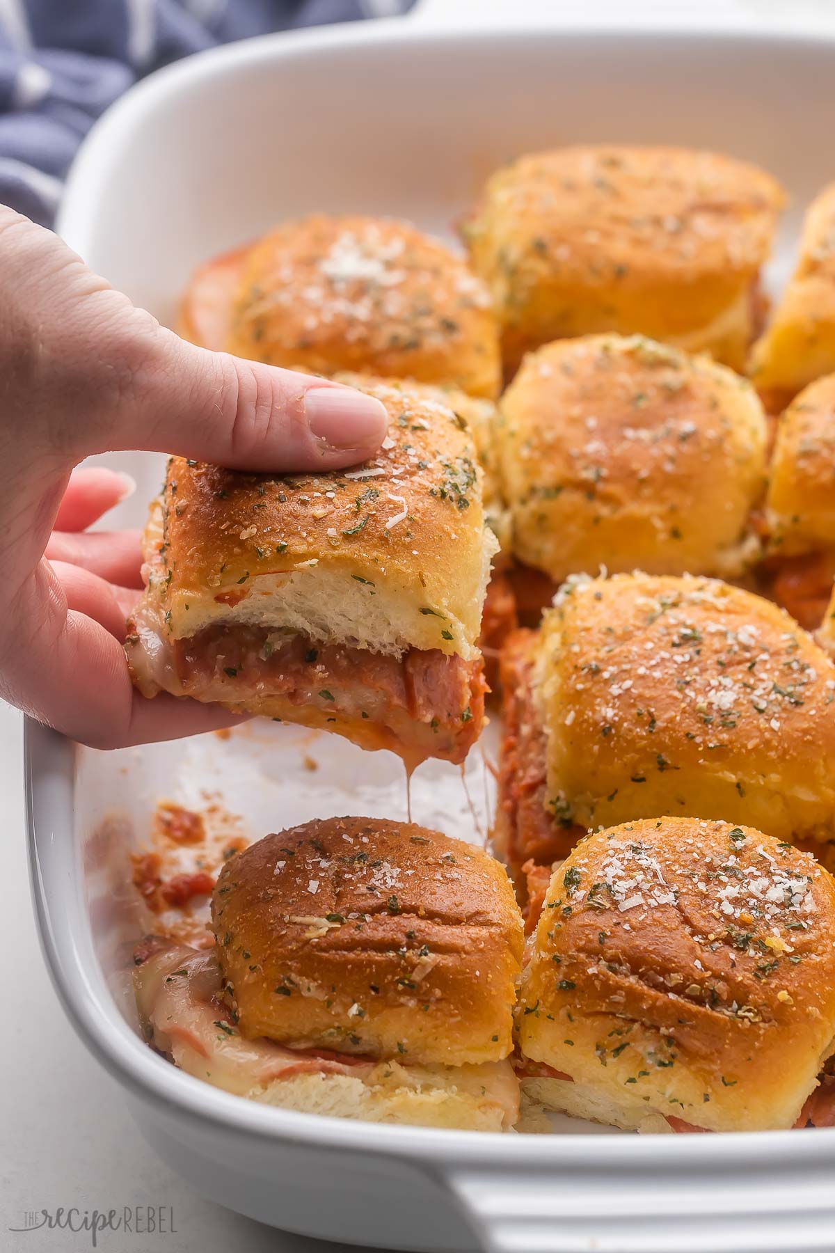 Pizza Sliders in a white dish with one slider being lifted by a hand.