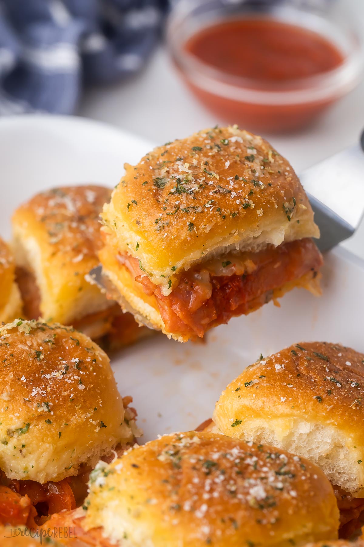 Pizza Sliders in a white dish with one slider being lifted using a spatula.