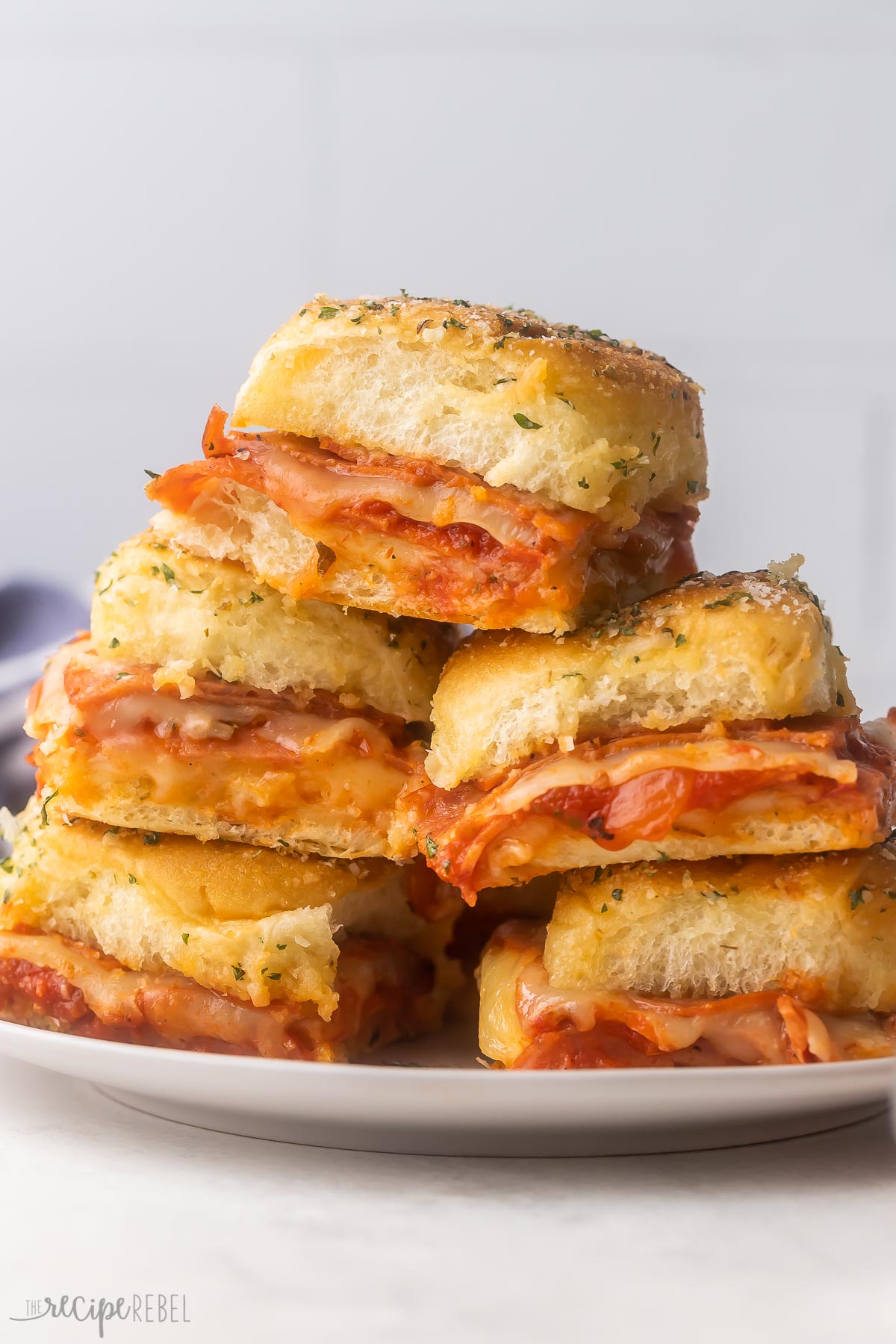 Pizza Sliders are made with soft dinner rolls, pizza sauce, melty mozzarella cheese, and pepperoni slices! They're quick to whip up and make the perfect appetizer or easy weeknight dinner. #sliders #dinner #recipe | dinner recipe | dinner ideas | easy recipe | pepperoni pizza | sandwich | sandwiches | picnic recipe | game day food | appetizer recipes Stack of pizza sliders on a plate.