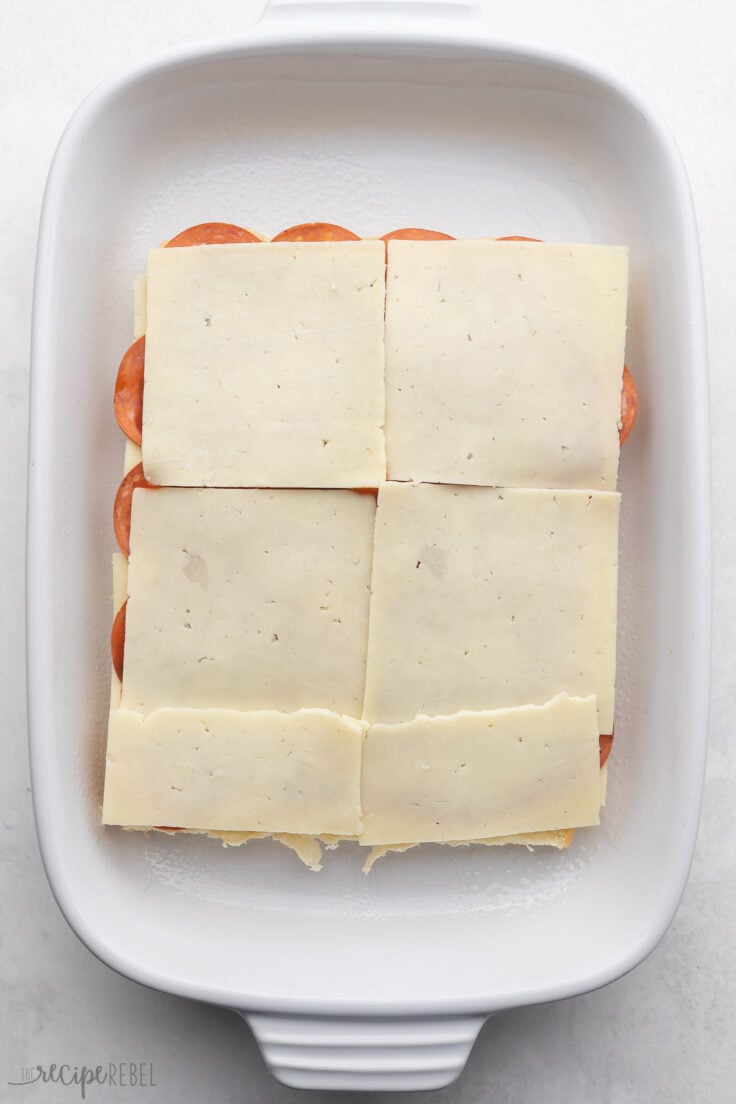A layer of cheese on top of the pepperoni on the slider rolls.