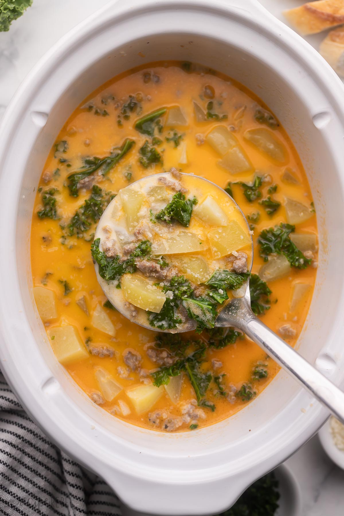 overhead image of metal ladle scooping slow cooker zuppa toscana from crockpot.