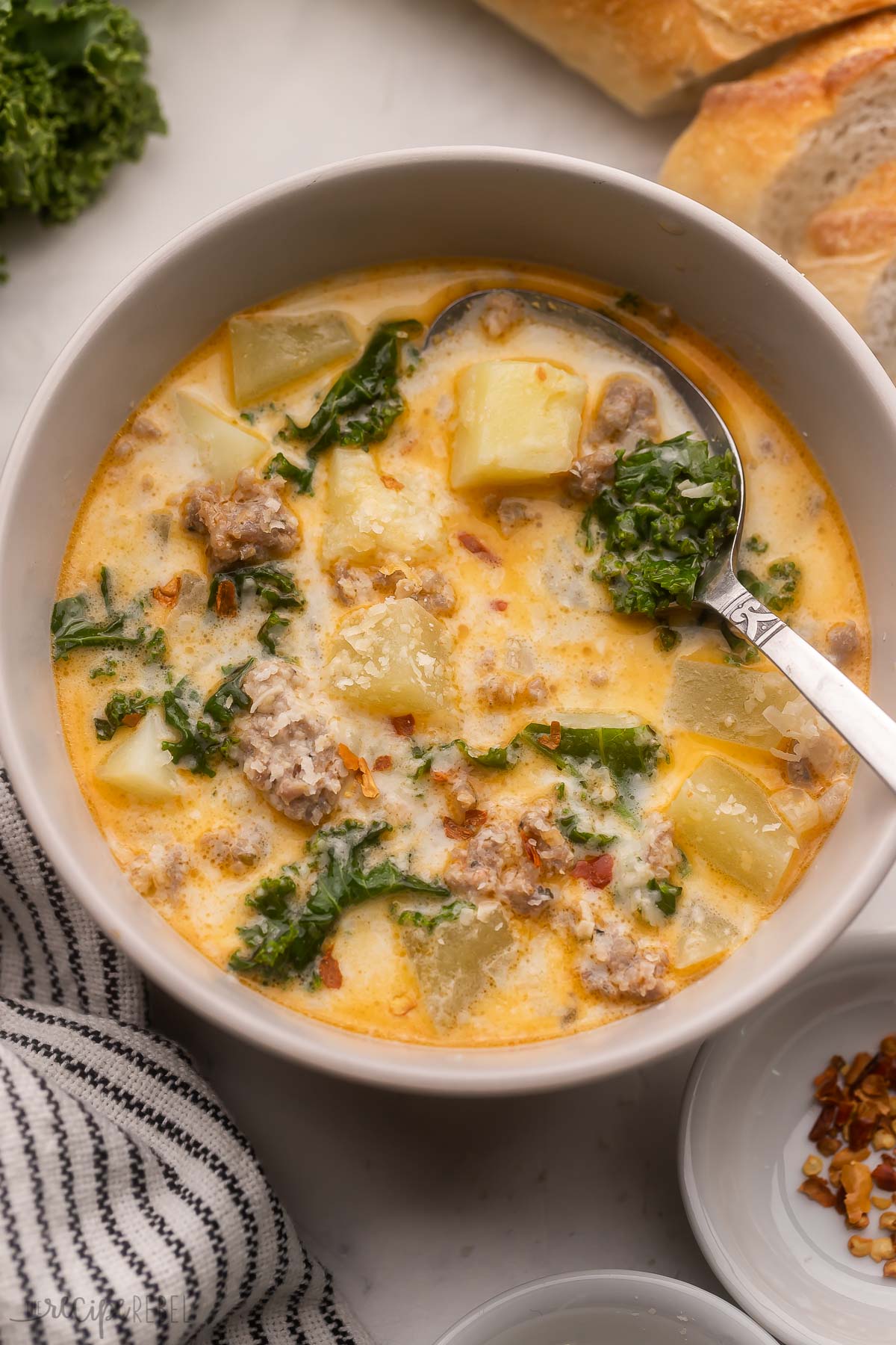 bowl of crockpot zuppa toscana with bread in the background and spoon in bowl.