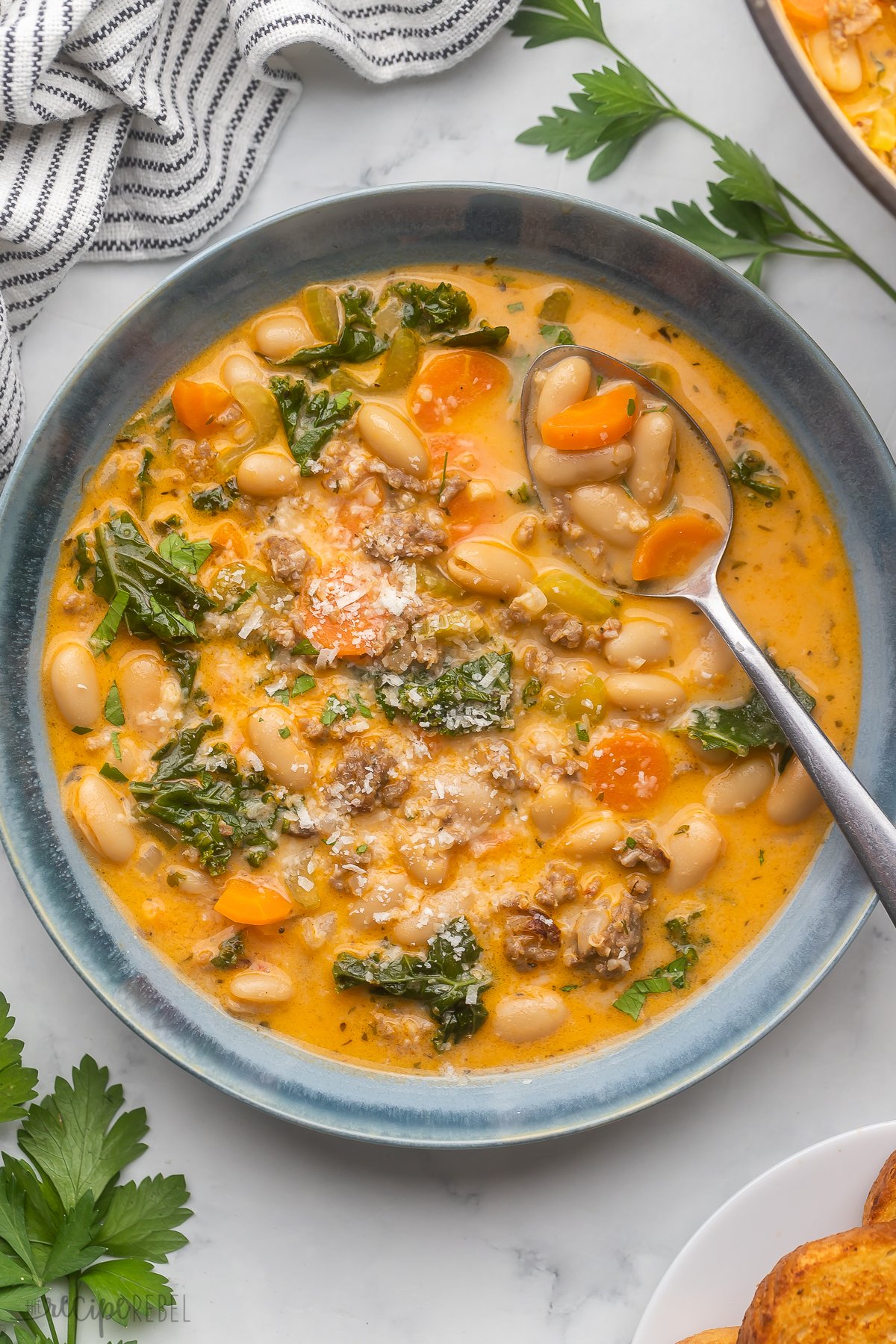 overhead image of tuscan white bean soup in a blue bowl with spoon.