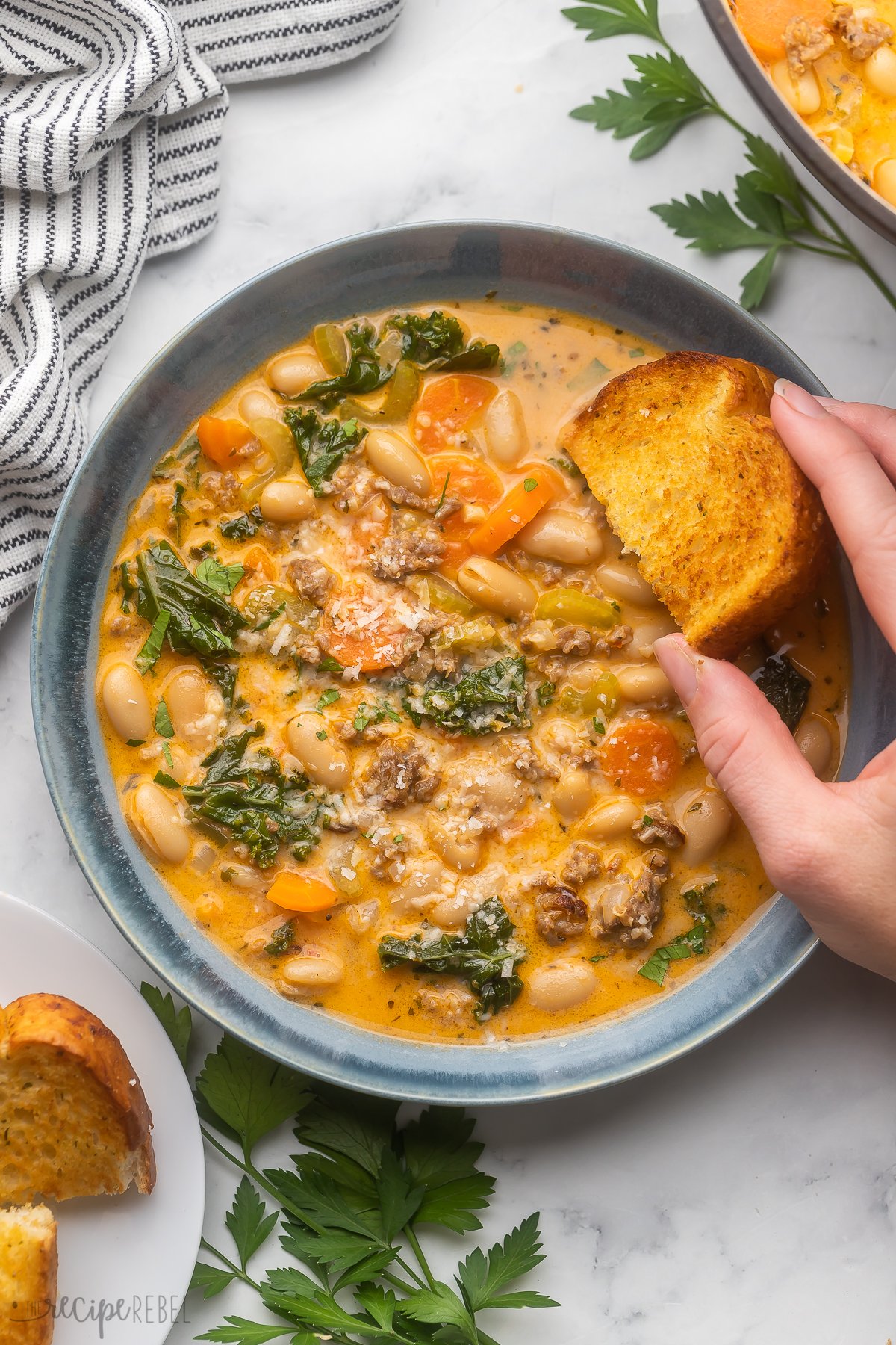 overhead image of hand dunking garlic toast into white bean soup.