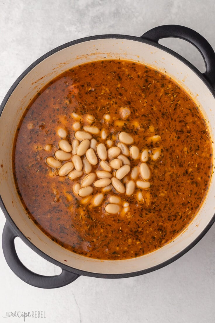 broth and beans added to white bean soup in pot.