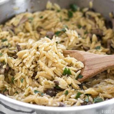 parmesan mushroom orzo in steel skillet with wooden spoon.