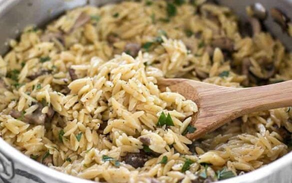 parmesan mushroom orzo in steel skillet with wooden spoon.