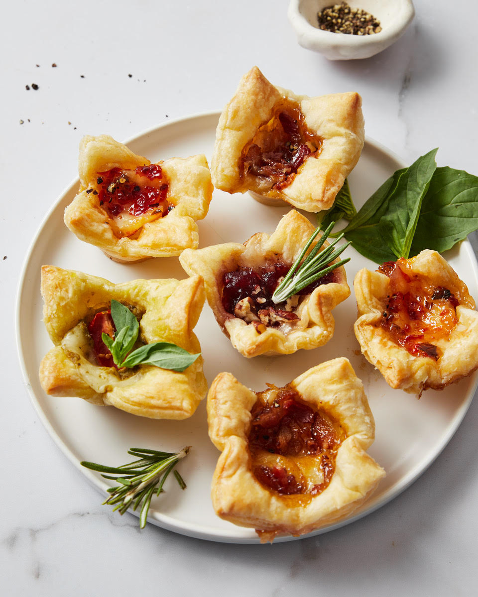 baked brie bites on a plate with fresh herbs on a white background.