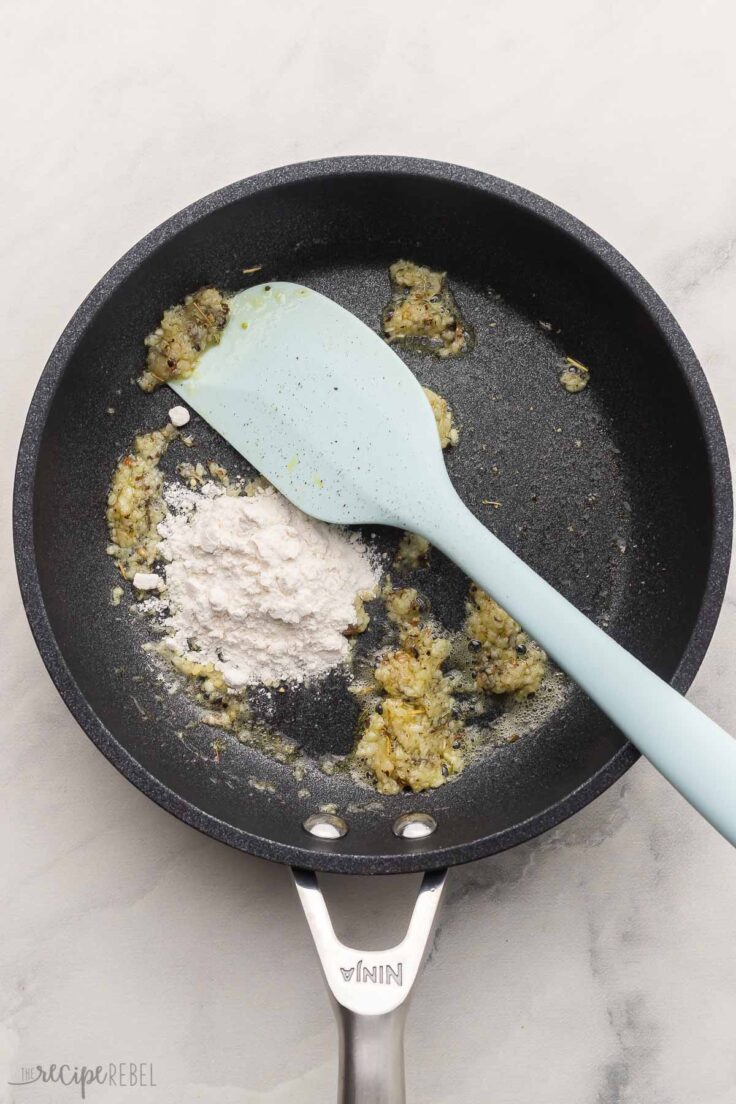 black frying pan and spatula with flour added to other ingredients.