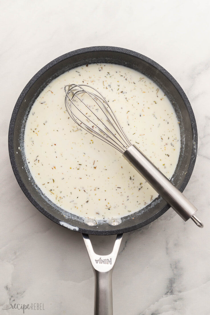 alfredo sauce in black frying pan with steel whisk.