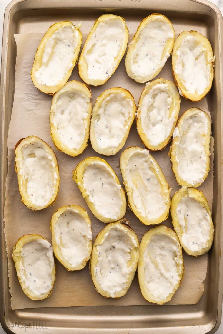 alfredo sauce spread in scooped out potatoes on sheet pan.