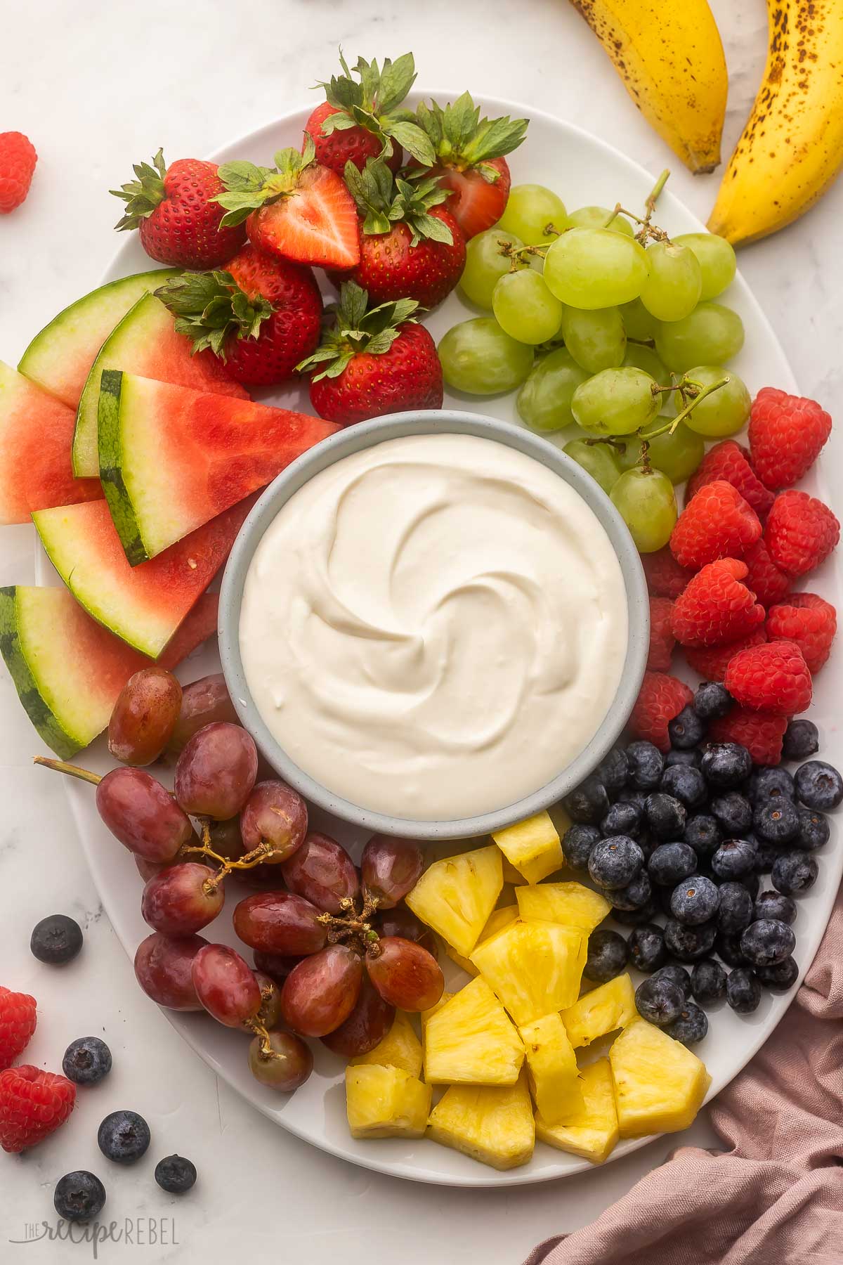 a white platter of fruit with cream cheese fruit dip in the centre.