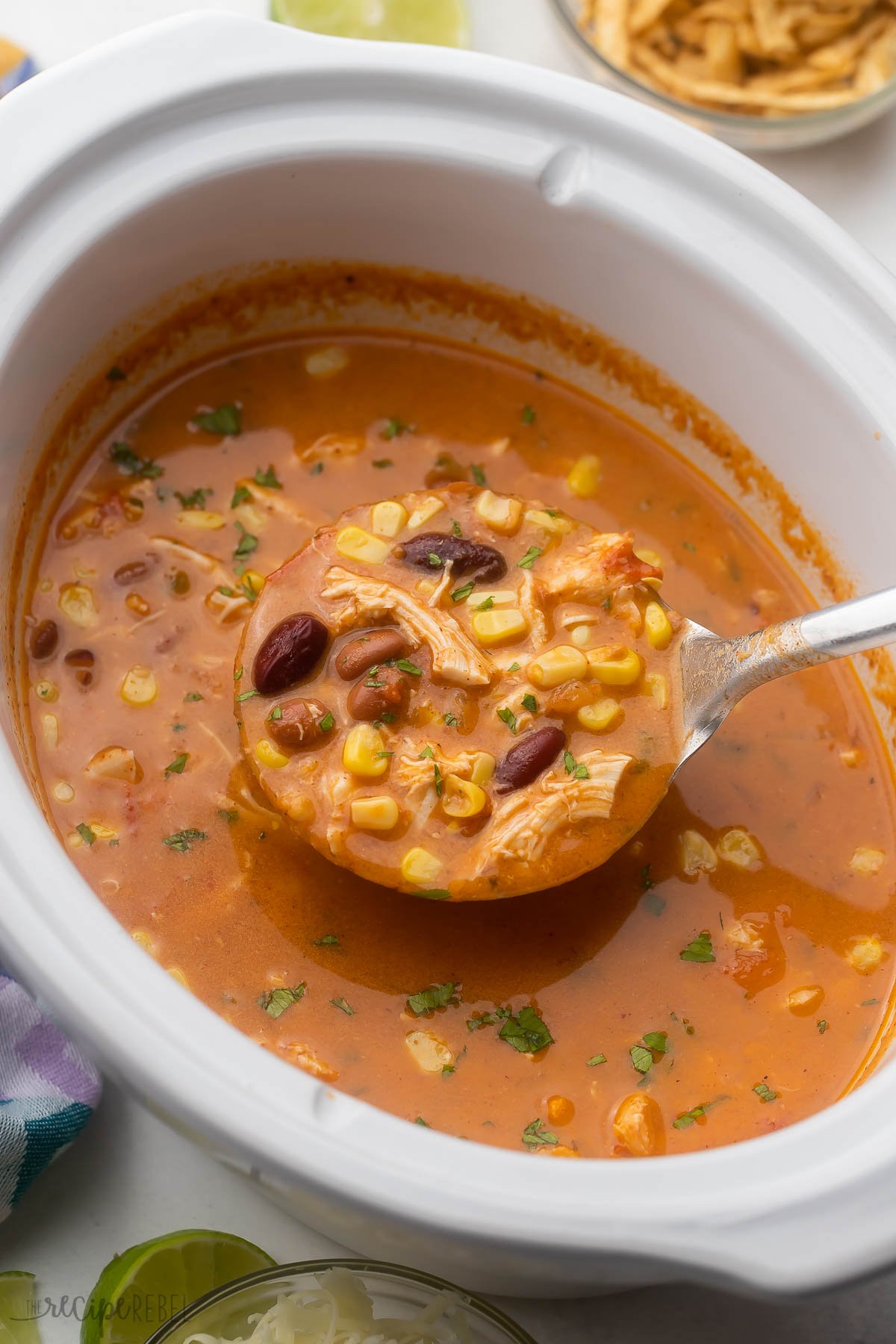 a steel ladle scooping chicken taco soup out of white slow cooker.