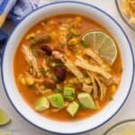 close up of a bowl of chicken taco soup with tortilla strips and avocado on top.