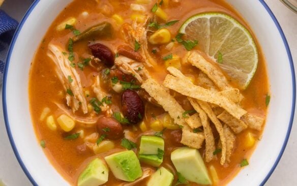 close up of a bowl of chicken taco soup with tortilla strips and avocado on top.