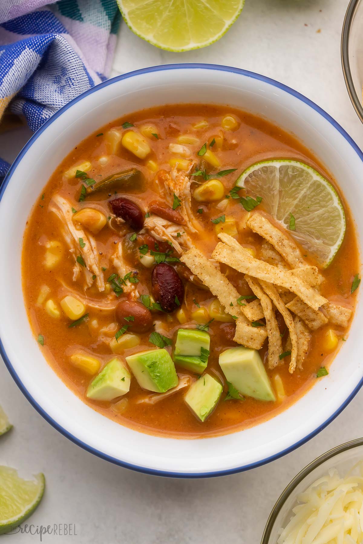 overhead view of a white bowl filled with chicken taco soup with garnishes beside.