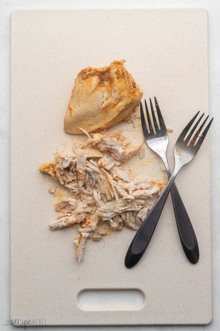 shredded chicken breast on cutting board with two forks beside.