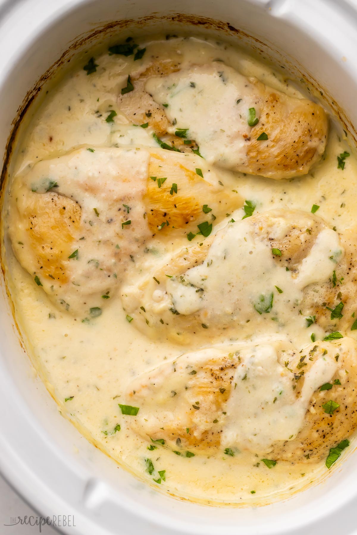 overhead image of chicken breasts in slow cooker with creamy garlic chicken.