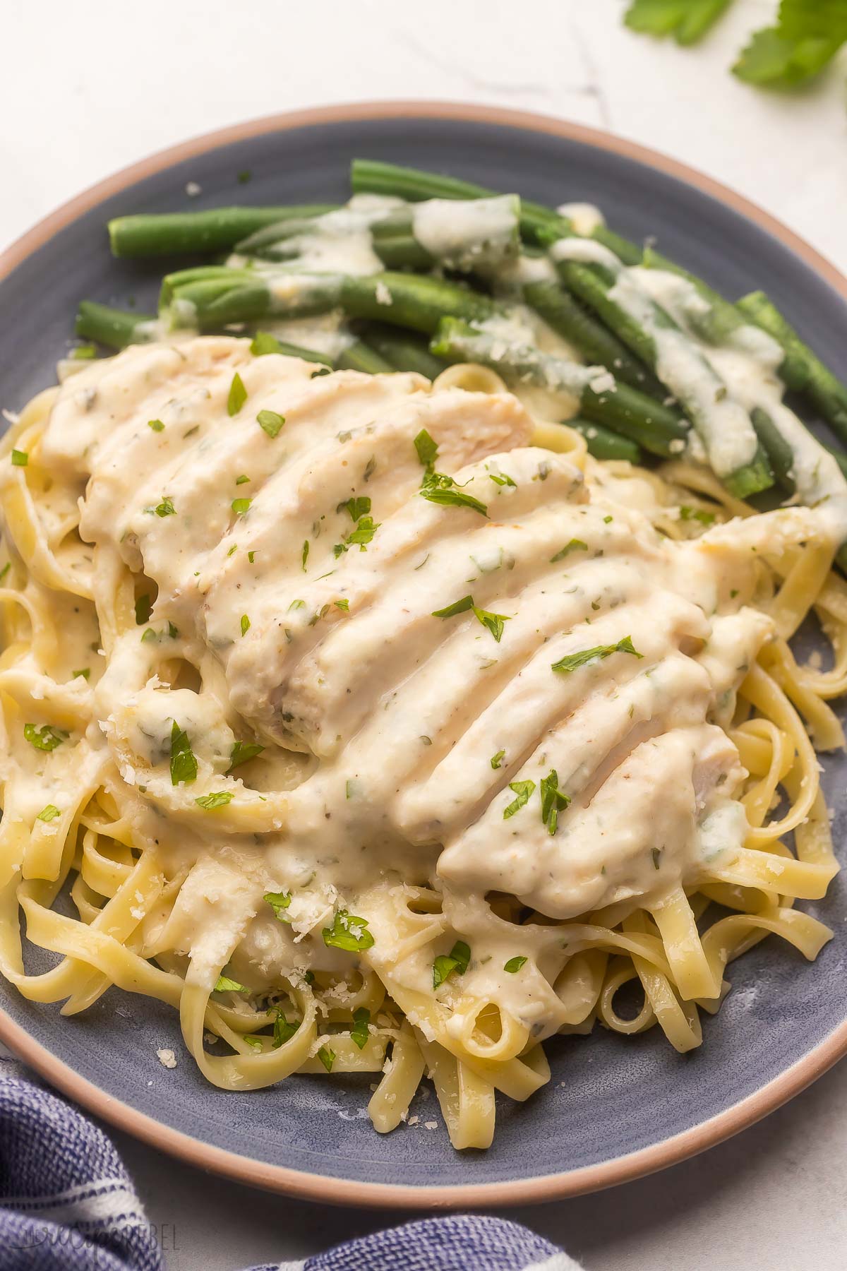 blue plate filled with green beans and pasta topped with creamy garlic chicken.