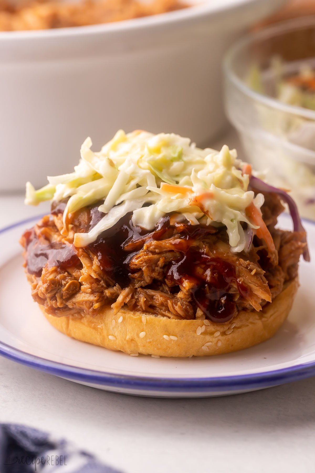 bun on a white plate topped with pulled pork and coleslaw.
