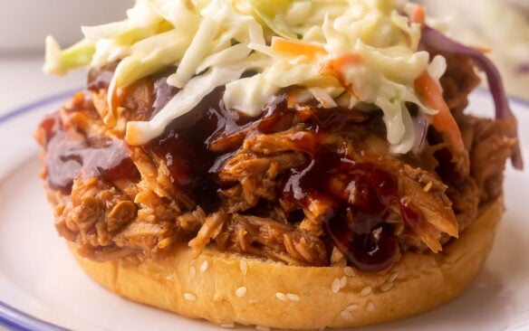 close up of bun topped with pulled pork, bbq sauce, and coleslaw.