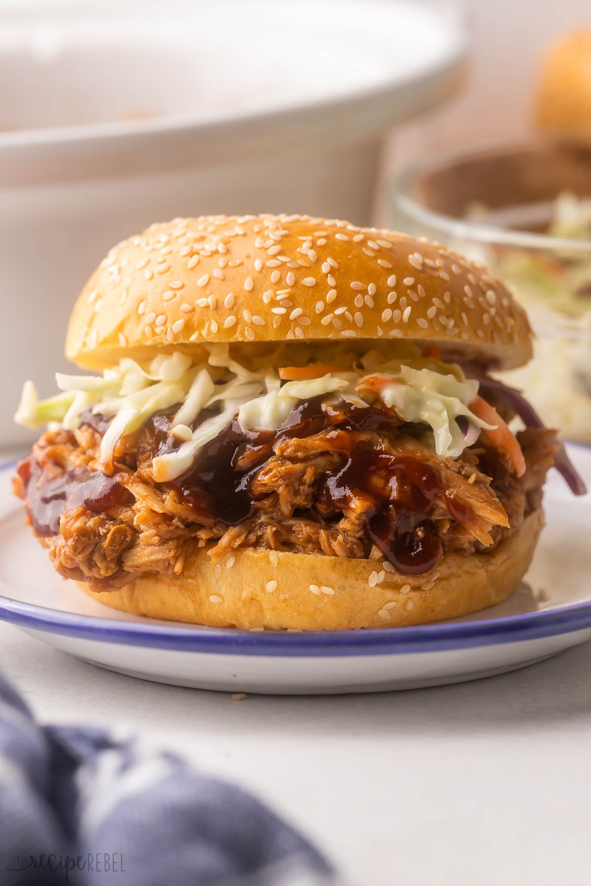 pulled pork sandwich topped with coleslaw on white plate.