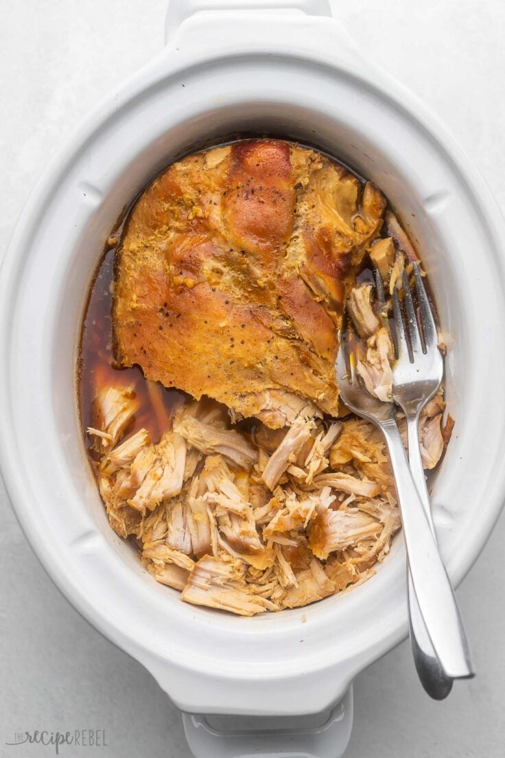 overhead view of crockpot with partially pulled pork and two forks.