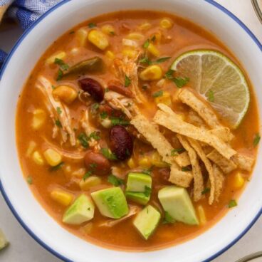 overhead view of a white bowl filled with chicken taco soup with garnishes beside.