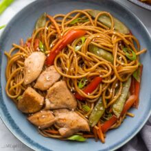 close up a blue dish filled with teriyaki chicken and noodles topped with sesame seeds.