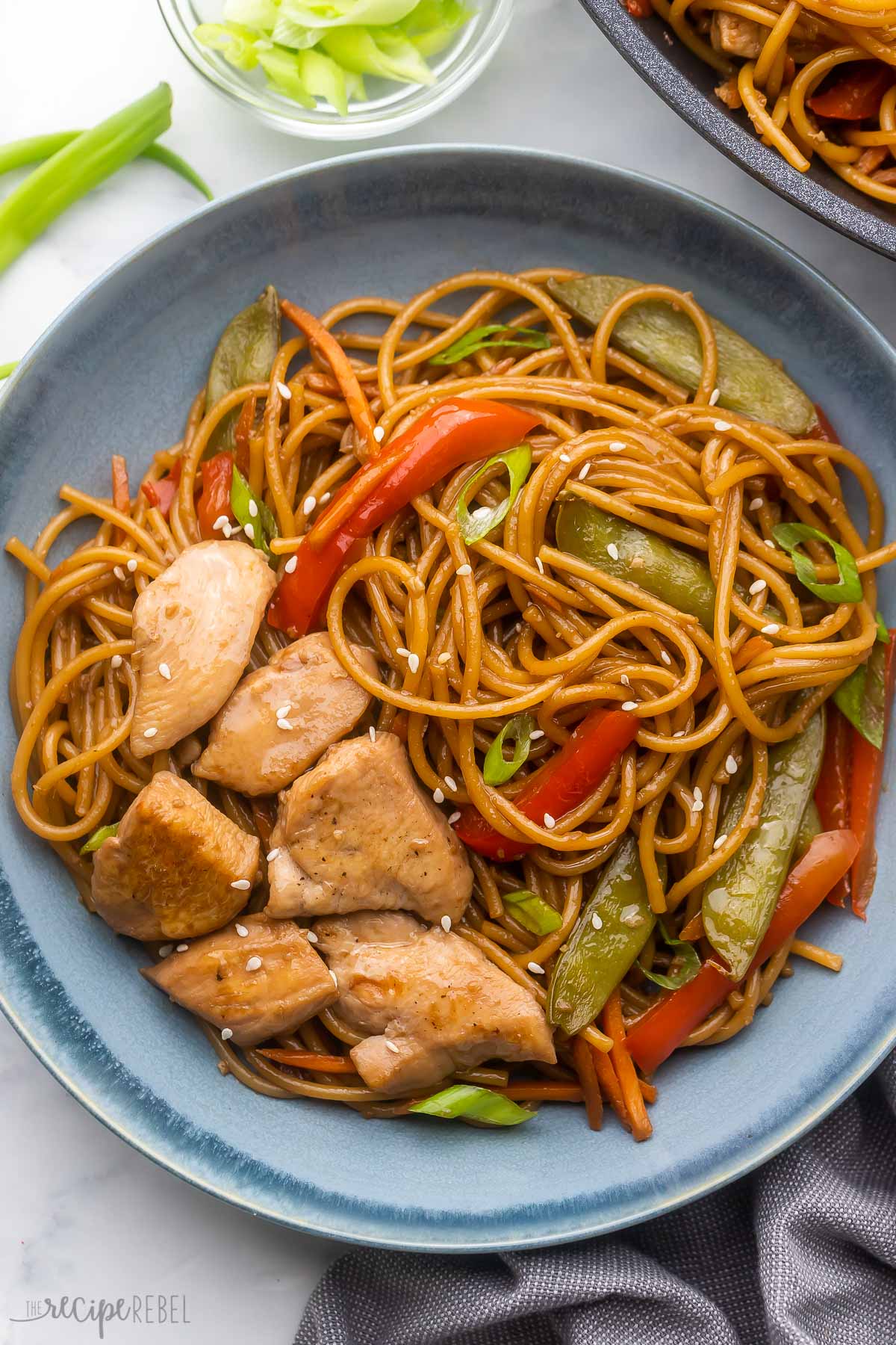 overhead shot of a blue dish filled with teriyaki chicken and noodles with green onions beside.