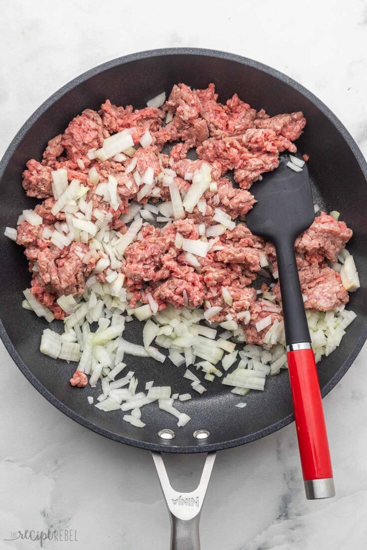 ground beef and onions in black frying pan with spatula beside.