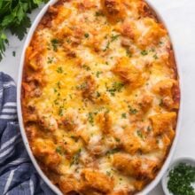 close up of rigatoni pasta bake in white dish with chopped parsley sprinkled on top.