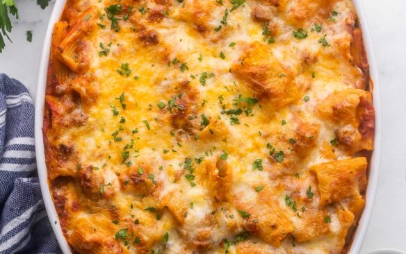 close up of rigatoni pasta bake in white dish with chopped parsley sprinkled on top.