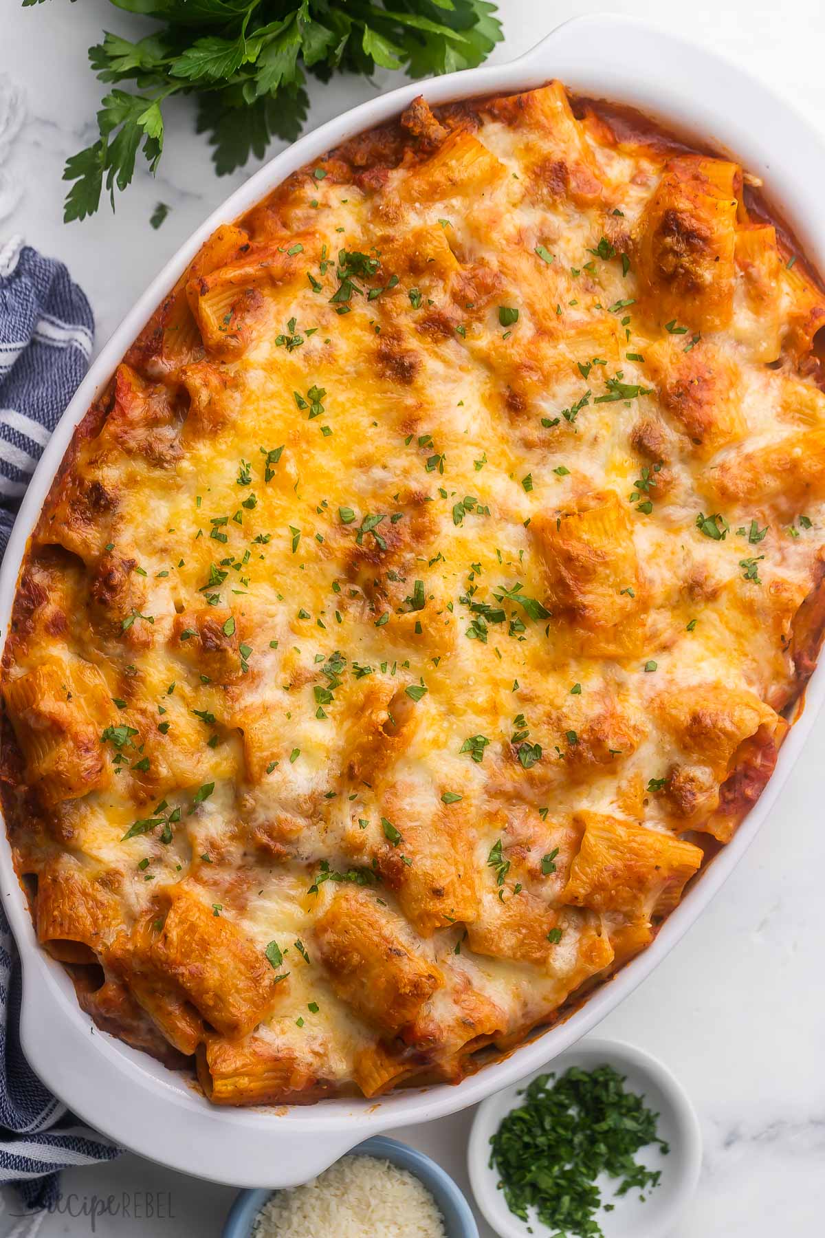 white baking dish filled with rigatoni pasta bake topped with chopped parsley on white surface.