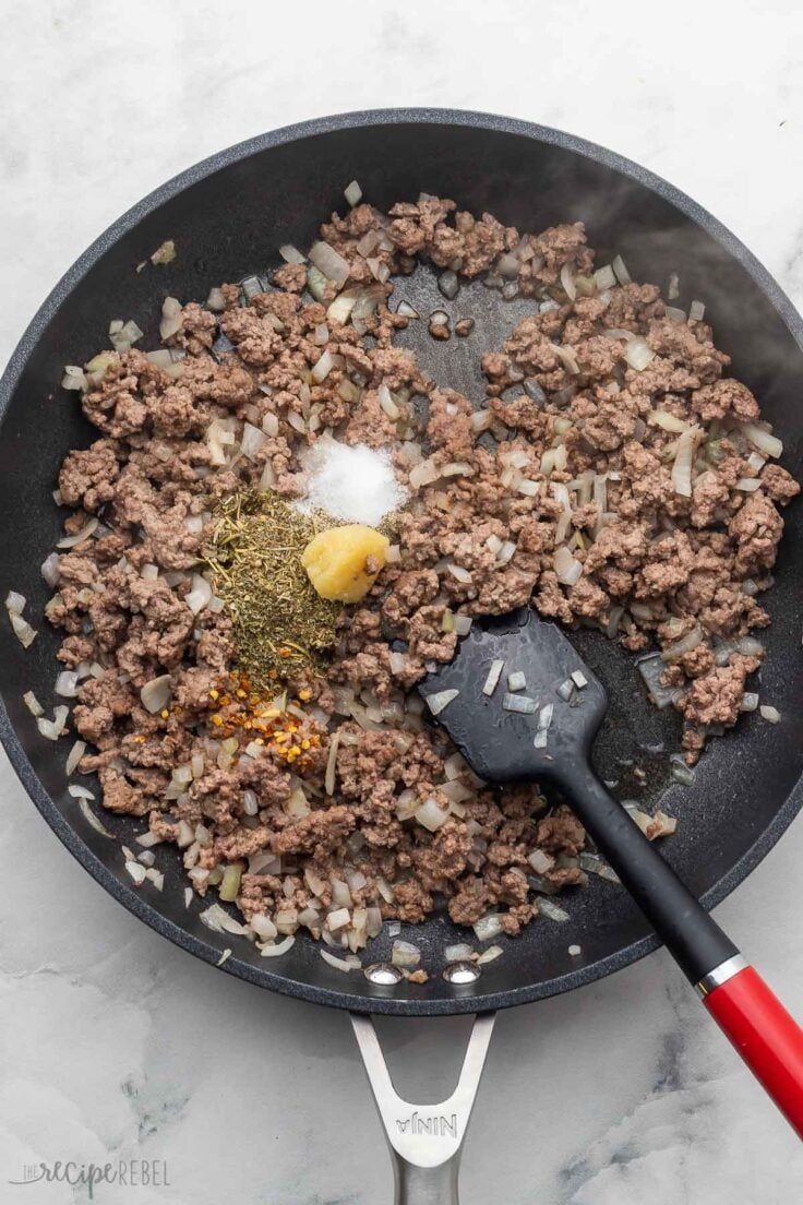 cooked ground beef in black frying pan with spices added.