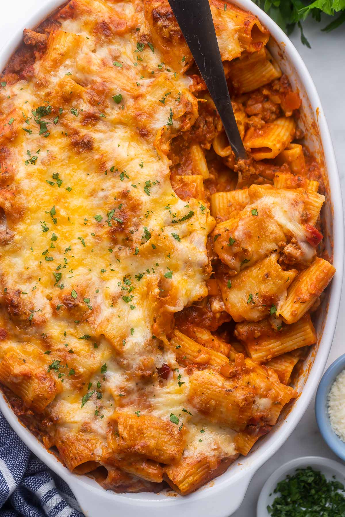 overhead view of a white dish filled with rigatoni pasta bake and a steel ladle.