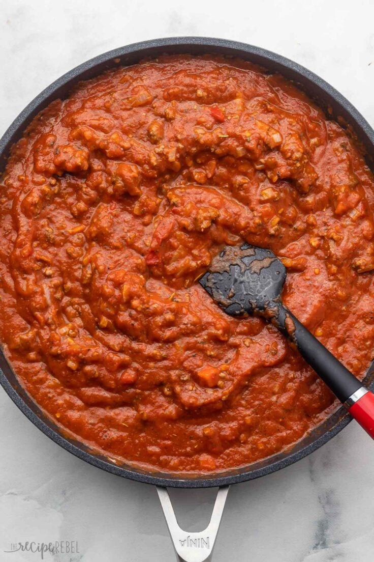 rigatoni pasta bake sauce in black frying pan on grey surface.