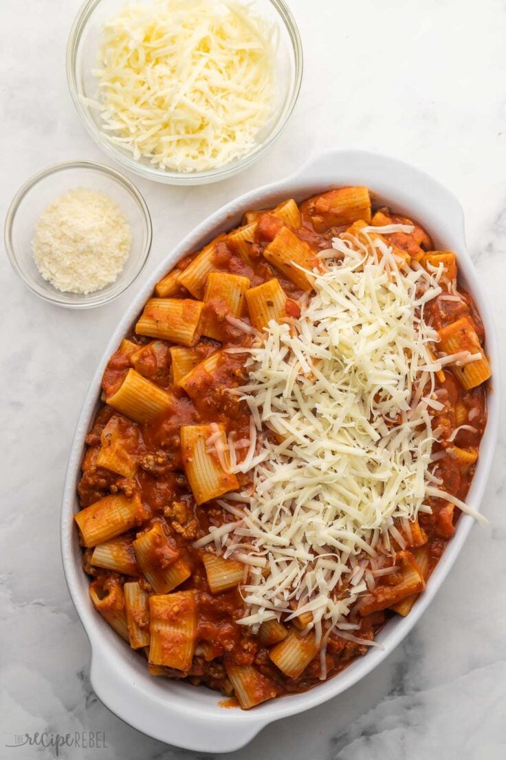 pasta and sauce in white baking dish with shredded cheese added on top.