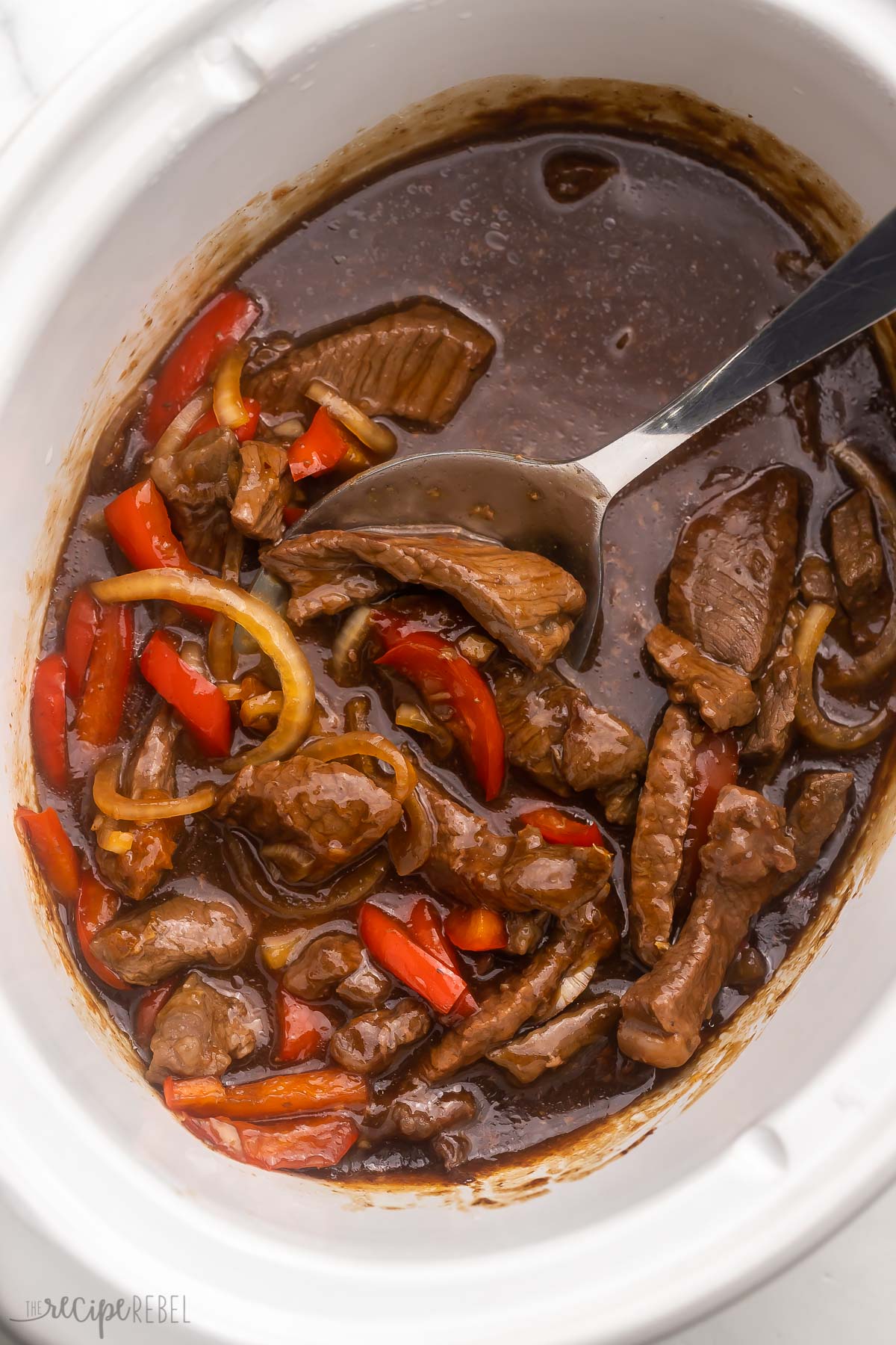 white slow cooker filled with mongolian beef and steel ladle.