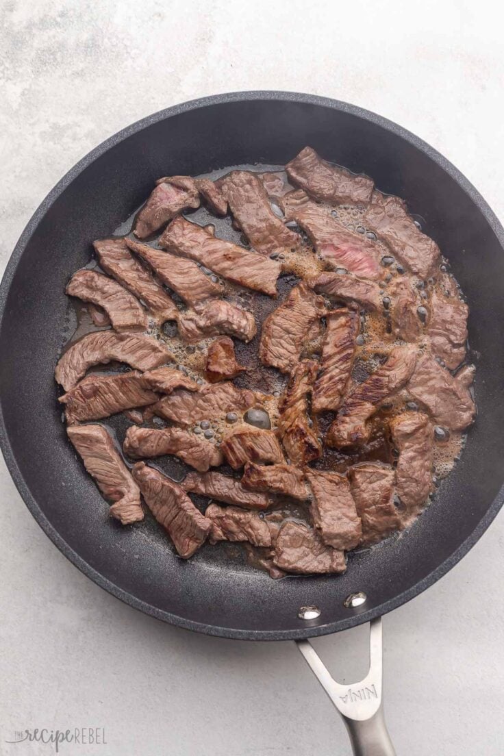 black frying pan with sliced beef cooking in it.