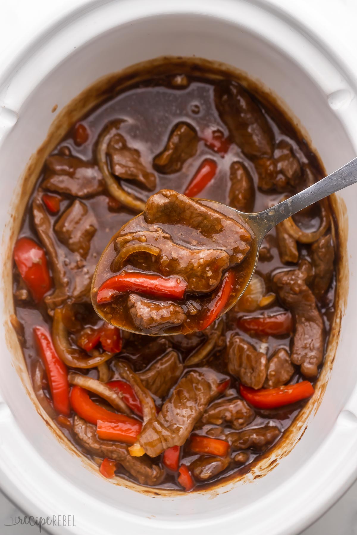 steel ladle scooping mongolian beef out of a white slow cooker.